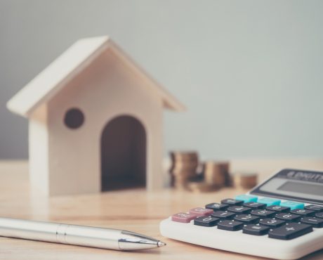 Calculator with wooden house and coins stack and pen on wood table. Property investment and house mortgage financial concept